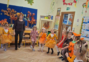Zdjęcie przedstawia dzieci z grupy III wraz z nauczycielką podczas wspólnego tańca w kole.