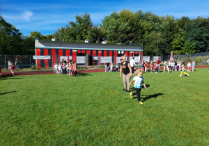 Zdjęcie przedstawia dzieci podczas zabaw sportowych - bieg do pachołka z przeskakiwaniem obręczy..