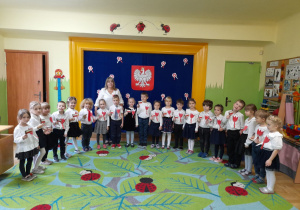 Zdjęcie przedstawia dzieci z grupy III - "Jagódki" wraz z nauczycielką przed odśpiewaniem hymnu.
