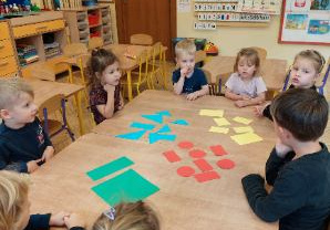 Zdjęcie przedstawia dzieci z grupy I i II podczas tworzenia zbiorów z użyciem figur geometrycznych.
