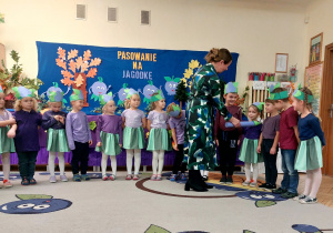 Zdjęcie przedstawia dzieci oraz panią Dyrektor, która magicznym ołówkiem pasuje kolejne dziecko na przedszkolaka.