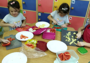 Zdjęcie przedstawia dzieci krojące ziemniaki i paprykę w kostkę.