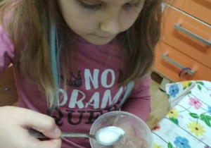 Na tym zdjęciu widać dziewczynkę z grupy IV, która sprawdza, czy substancja wymieszana z wodą rozpuściła się.