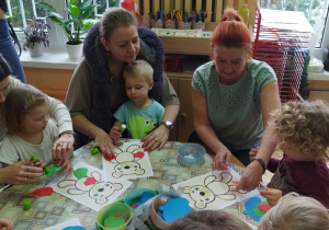 Zdjęcie przedstawia nauczycielkę, rodziców oraz dzieci wykonujące pracę plastyczą