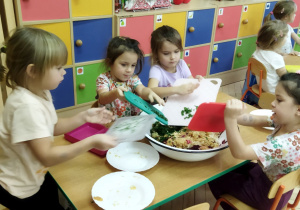 Zdjęcie przedstawia dziewczynki, które przesypują posiekaną natkę z pietruszki do miski.