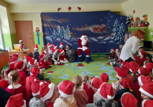 Na tym zdjęciu widać dzieci z mikołajowych czapkach na spotkaniu z Mikołajem.