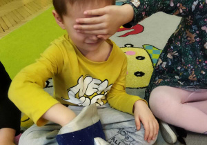 Zdjęcie przedstawia dzieci podczas zabawy, w której dzieci odgadują dotykiem, jakie prezenty zgubił Mikołaj.