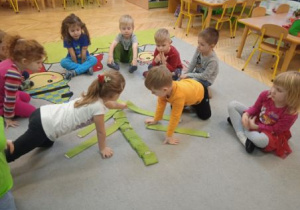 Zdjęcie przedstawia dzieci układające choinkę z szarf i woreczków w kolorze zielonym.