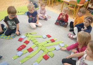 Zdjęcie przedstawia dzieci układające choinkę z szarf i woreczków w kolorze zielonym oraz ozdób z kolorowych worczków.