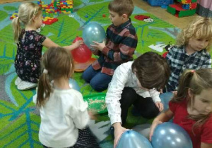 Zdjęcie przedstawia dzieci wykonujące doświadczenia z balonami oraz z drobnymi materiałami.