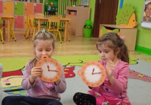 Zdjęcie przedstawia dziewczynki z grupy II podczas zabawy utrwalającej cyfry na tarczy zegara.