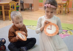 Zdjęcie przedstawia dziec podczas zabawy utrwalającej cyfry na tarczy zegara.
