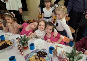 Zdjęcie przedstawia dziewczynki przy stole podczas poczęstunku.