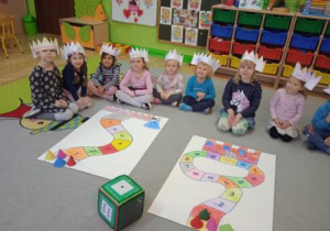 Zdjęcie przedstawia dzieci z grupy I i II siedzacych przed planszami gry, w koronach na głowach wykonanych przez siebie.