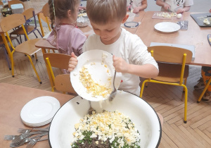 Na tym zdjęciu widać Stasia, który przesypuje z talerza do miski pokrojone jajka.
