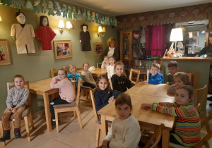 Zdjęcie przedstawia dzieci z grupy IV przy stolikach w kawiarence.