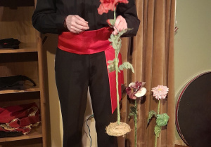 Zdjęcie przedstawia aktora prezentującego rekwizyty użyte w przedstawieniu - kwiaty.
