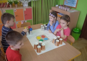 Na tym zdjęciu widać dzieci z grupy I i II grającew grę planszową, w której wykorzystane zostały kubki jednorazowe oraz kolorowe piłeczki.