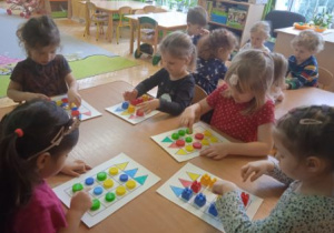Na tym zdjęciu widać dzieic z grupy I i II grajace w grę planszową z wykorzystaniem kolorowych klocków.