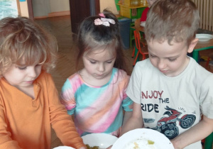 Zdjęcie przedstawia dzieci przesypujące pokrojone składniki do miski.