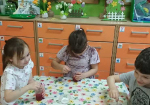 Zdjęcie przedstawia Maję, Michalinę i Krystiana z grupy IV, którzy dodają barwnik do solalnki.