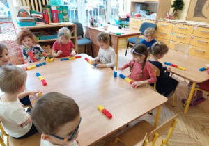 Zdjęcie przedstawia dzieci podczas układania kodu matematycznego z kolorowych klocków.