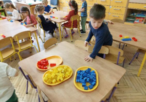 Zdjęcie przedstawia dzieci układjace kod matematyczny z klocków w trzech kolorach.