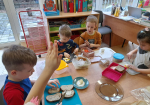 Zdjęcie przedstawia dzieci krojące na plasterki jajka oraz smarujące pieczywo masłem.