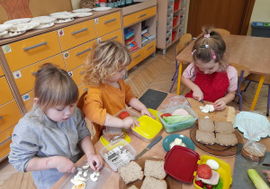 Zdjęcie przedstawia Olę, Hanię N. i Filipa przygotowujących dodatki do kanapek.