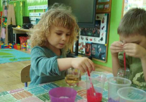 Zdjęcie przedstawia Filipa i Adriana, którzy zakraplają barwnik do kubków z płynem.