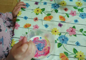 Na tym zdjęciu widać, jak jedno z dzieci miesza barwnik na powierzchni mleka.