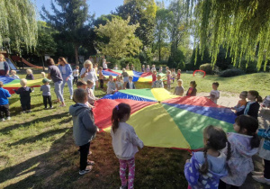 Zdjęcie przedstawia dzieci wraz z paniami podczas zabaw z chustami animacyjnymi.