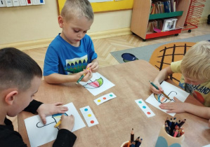 Zdjęcie przedstawia chłopców z grupy II kolorujących parasole według podanego kodu.