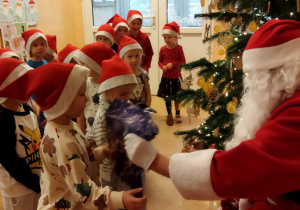 Zdjęcie przedstawia dzieci i Mikołaja wręczającego dzieciom upominki.