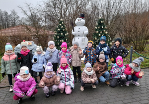 Zdjęcie przedstawia dzieci stojące przed bałwankiem.