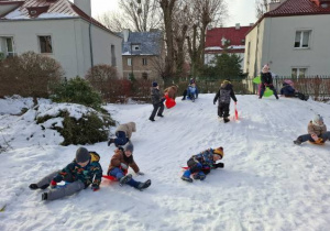 na tym zdjeciu widać kilku chłopców, którzy zjechali z górki oraz inne dzieci bawiące się na niej.