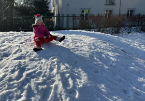 Zdjęcie przedstawia jedną z dziewczynek zjeżdżającą z górki na jabłuszku.