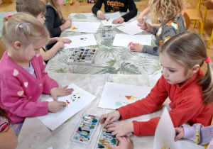 Zdjęcie przedstawia dzieci malujące pastelami ilustrację do bajki o Kubusiu Puchatku.