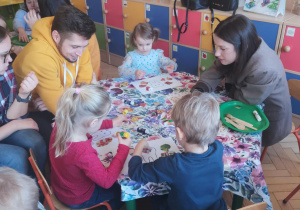 Zdjęcie przedstawia dzieci wykonujące pracę plastyczną w towarzystwie rodziców.