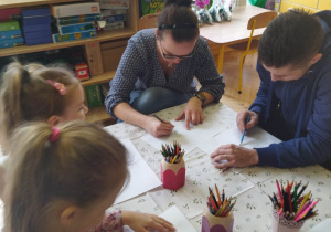 Zdjęcie przedstawia dwoje rodziców i dwie dziewczynki rysujące na temat "Kim będę, kiedy dorosnę?".