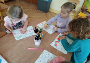 Na tym zdjęciu widać dwie dziewczynki i chłopca, którzy kolorują wzory na planszy według podanego rytmu.