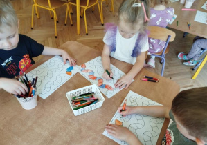 Na tym zdjęciu widać dwóch chłopców i dziewczynkę kolorujących wzory na planszy według podanego rytmu.