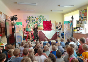 Zdjęcie przedstawia dzieci oglądające przedstawienie oraz aktorów z kukiełkami na scenie.