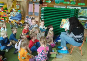 Zdjęcie przedstawia panią bibliotekarkę czytajacą dzieciom książeczkę.