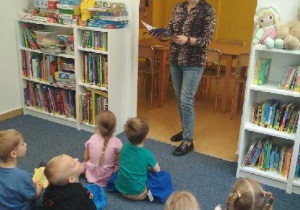Na tym zdjęciu widać panią bibliotekarkę czytającą książeczkę oraz dzieci.