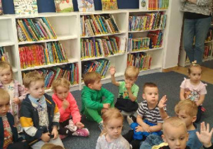 Zdjęcie przedstawia dzieci słuchające, jak należy korzystać z księgozbioru bibliotecznego.