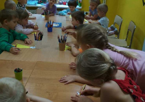 Zdjęcie przedstawia dzieci ozdabiające wykonane z papieru żyrafy.