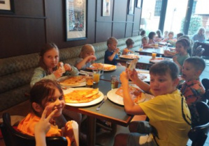 Zdjęcie przedstawia dzieci podczas spożywania pizzy we włoskiej pizzerii.