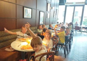 Zdjęcie przedstawia dzieci podczas spożywania pizzy we włoskiej pizzerii.