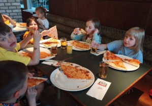 Zdjęcie przedstawia dzieci podczas spożywania pizzy we włoskiej pizzerii.
